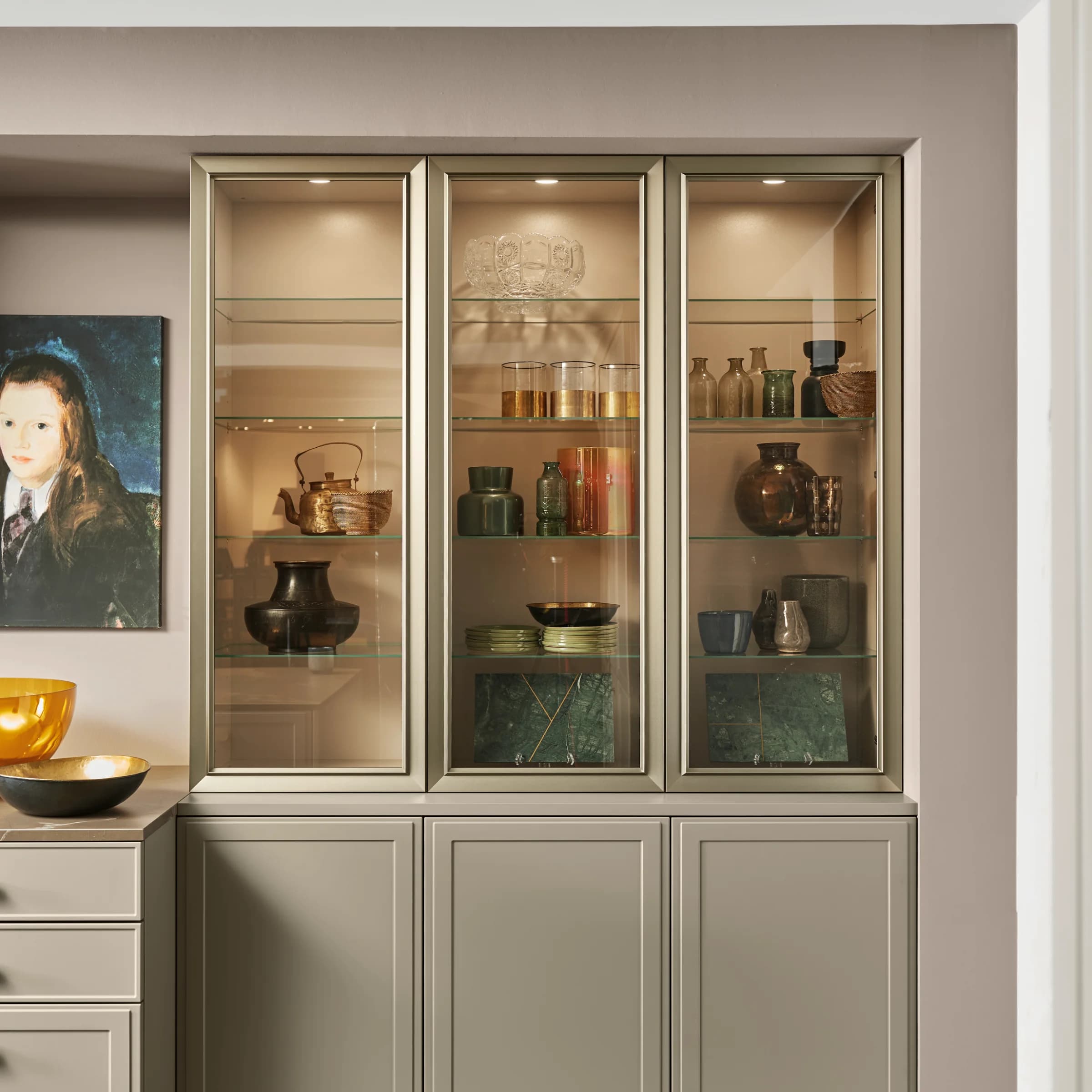 A stylish sideboard with a glass display, decorated with dishes and art, by Nolte Living.